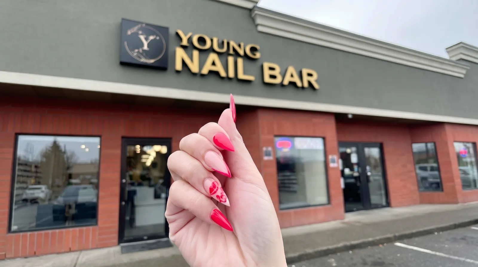 Manicured nails held up in front of the Young Nail Bar storefront